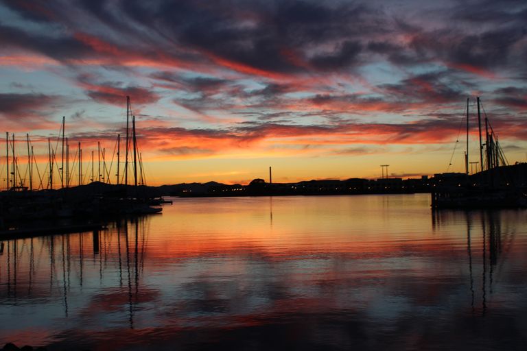 A stunning sunset over a harbor with sailboats, reflecting vibrant sky colors on the water.